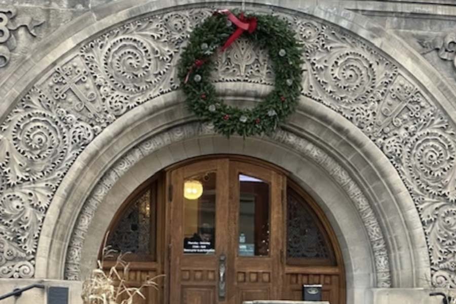 A stone arch in a gray bulding with a christmas wreath above the arch.