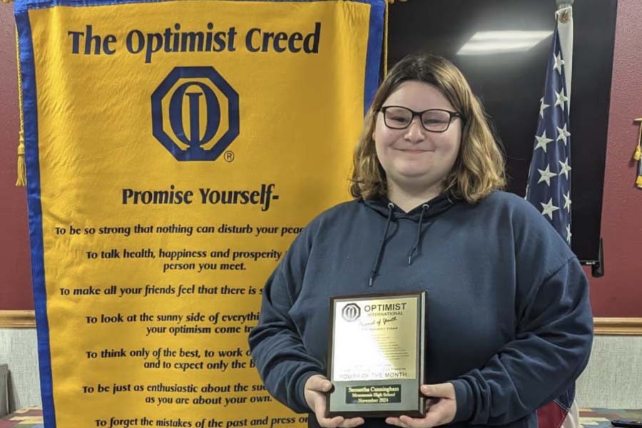 High school student standing in front of a banner while holding a trophy.