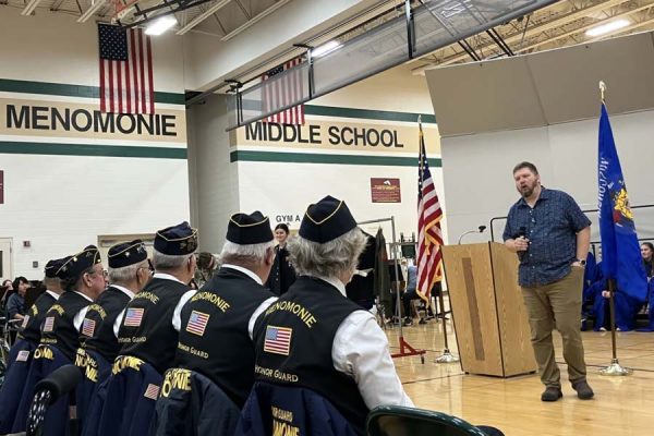 A man speaking to a group of veterans and middle school students.