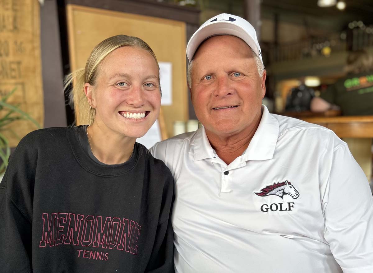 Daughter and father, Lexi Hastings and Jeff Hastings, are both head coaches at Menomonie High School. Lexi, left, is sporting a black sweatshirt the reads Menomonie Tennis in the color maroon, while Jeff wears a white polo shirt with the Mustangs logo and GOLF appearing.