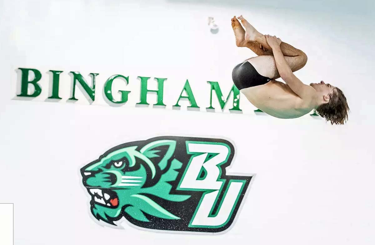 Menomonie's Dylan Norby dives at Binghamton University with a green Bearcat logo in the background.
