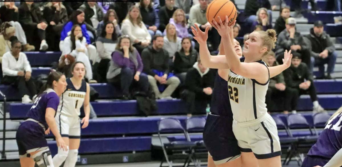 A women's basketball player in a white uniform shoots the ball towards the basket.