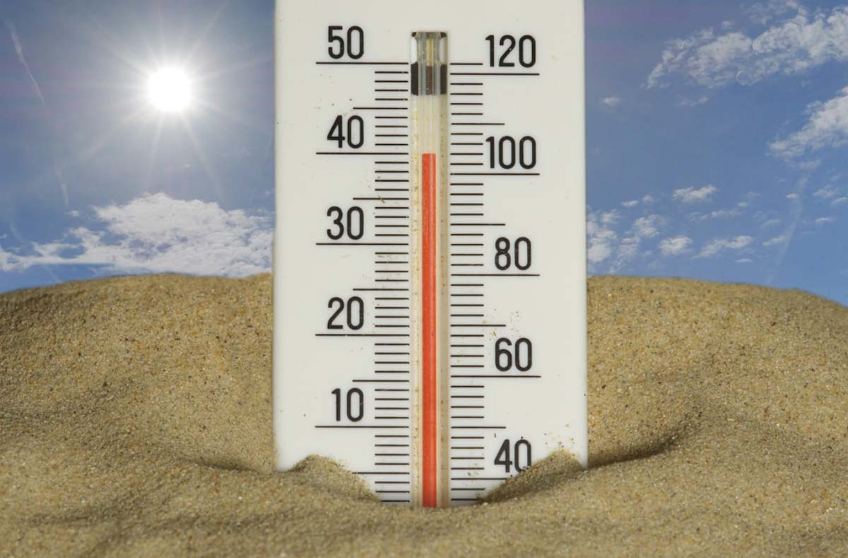 photo of thermometer stuck in the sand with the temperature reaching 100 degrees. Sun in the background