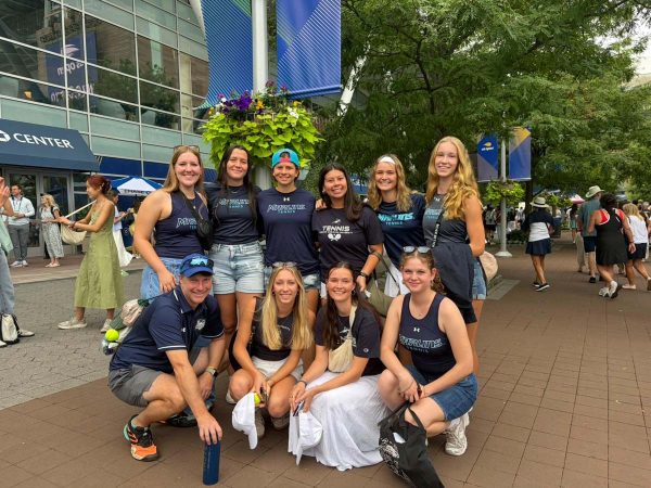 A collegiate women's tennis team gathers for a group photo at the US Open stadium.